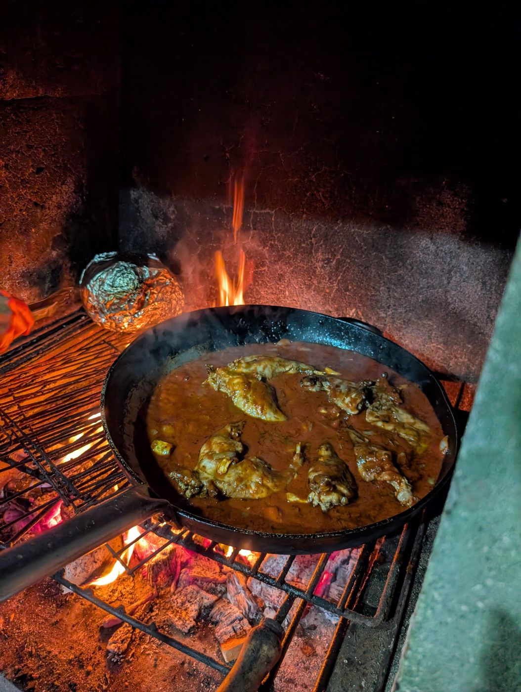 A pan of slow-cooked stew over an open wood fire at night