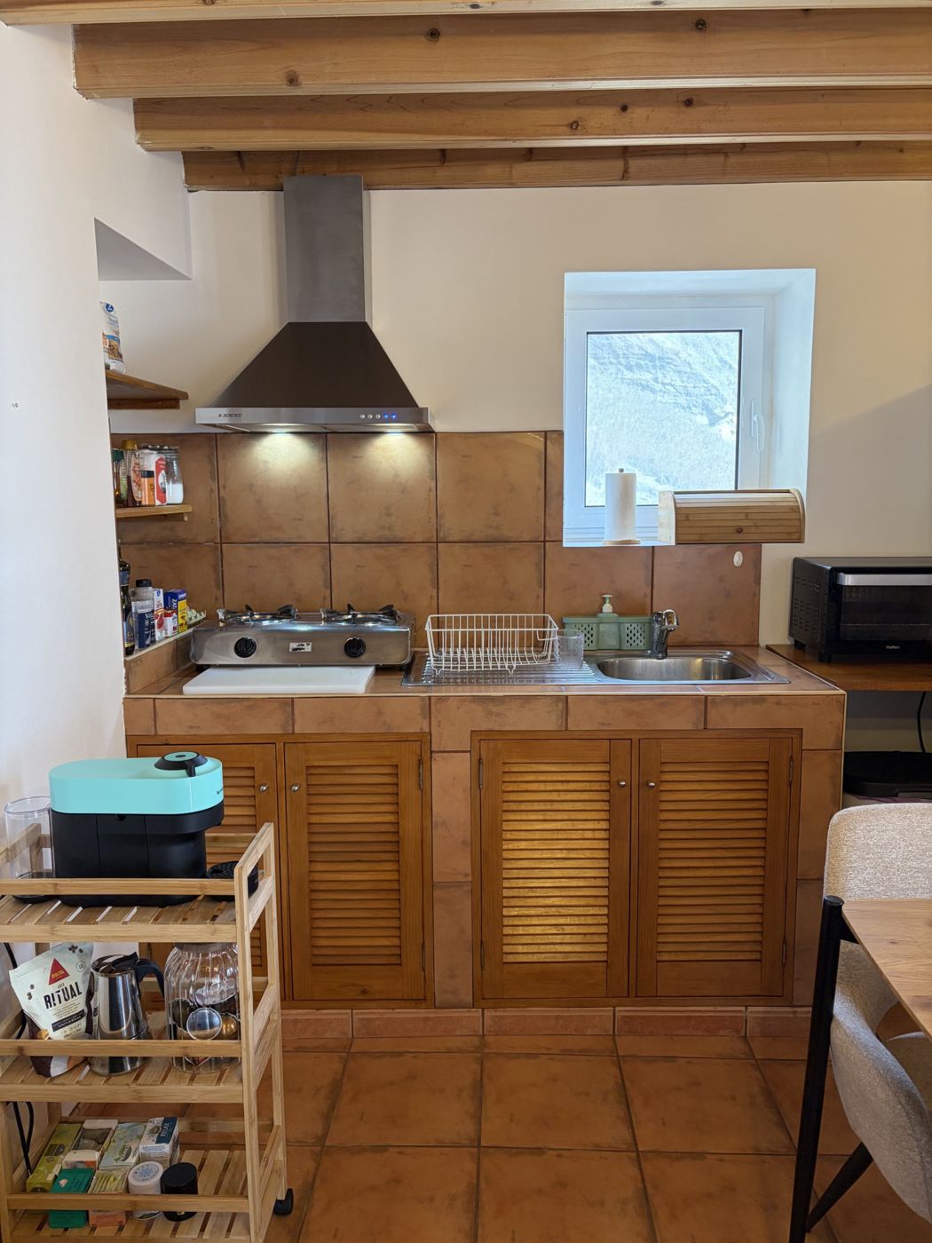 Kitchen with louvred wood cabinets, two-burner stove and a window onto the cliff