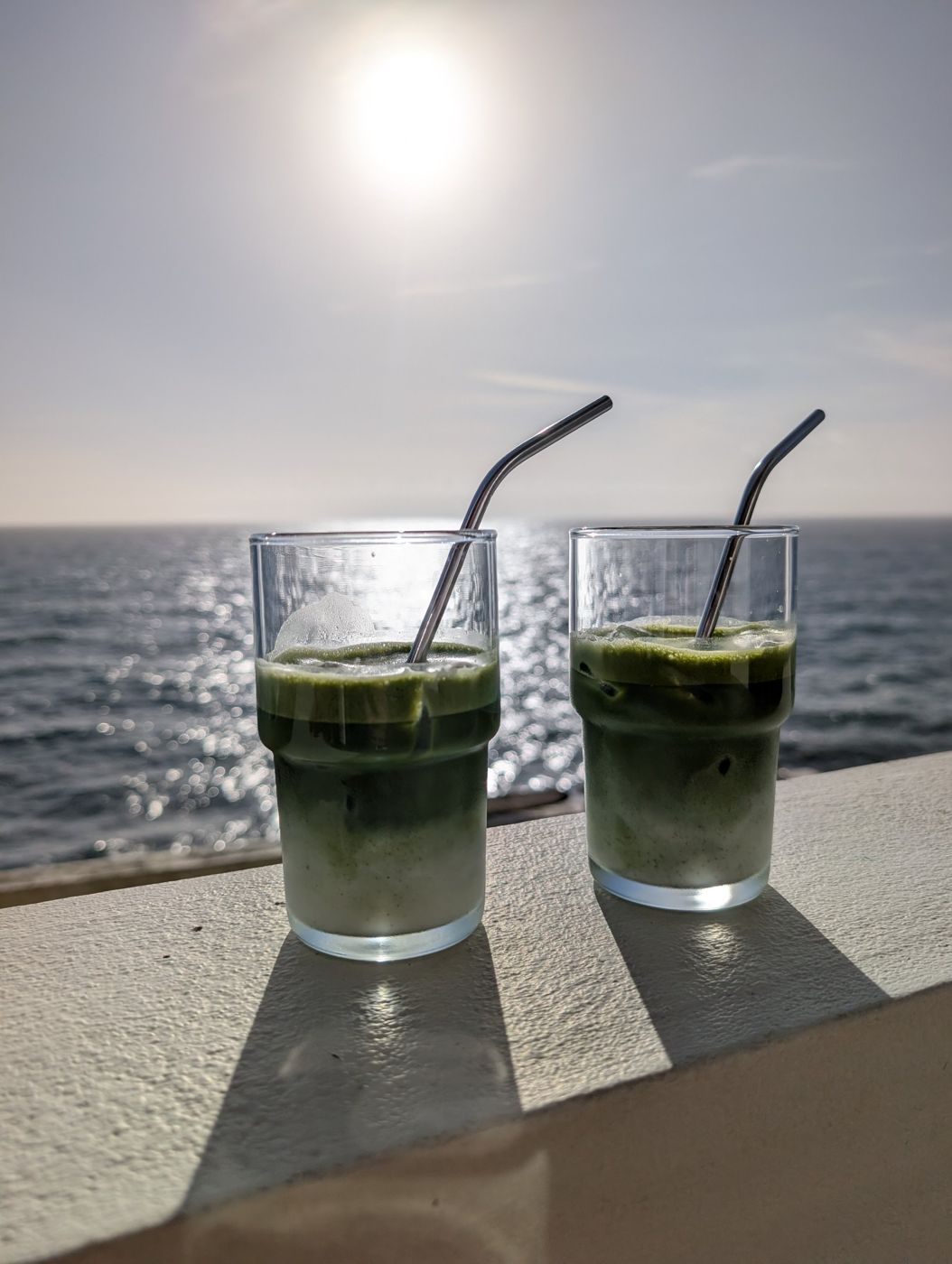 Two iced matchas on a white wall above the sea in winter sun