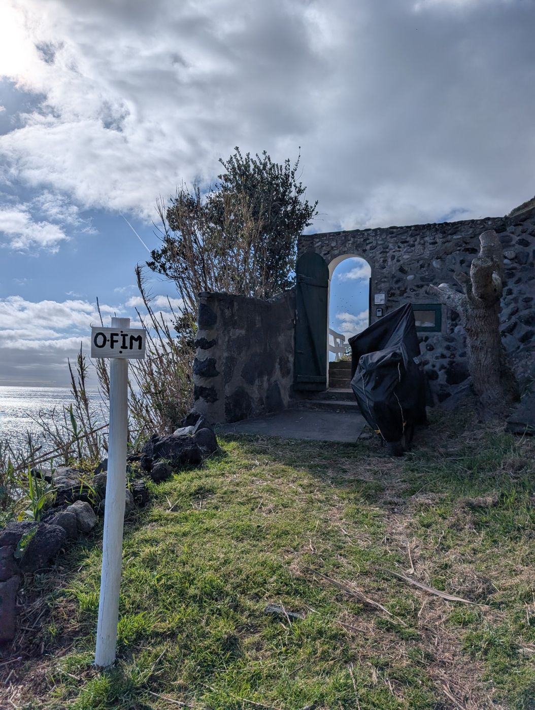 Hand-painted O FIM sign beside the arched gate, the sea behind
